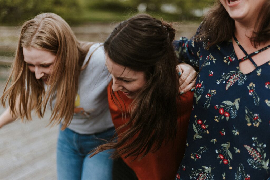 Trois femmes riant ensemble, les bras autour des épaules les unes des autres.