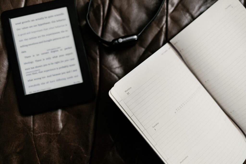Un agenda, un Kindle, et une montre posés sur un canapé en cuir marron.