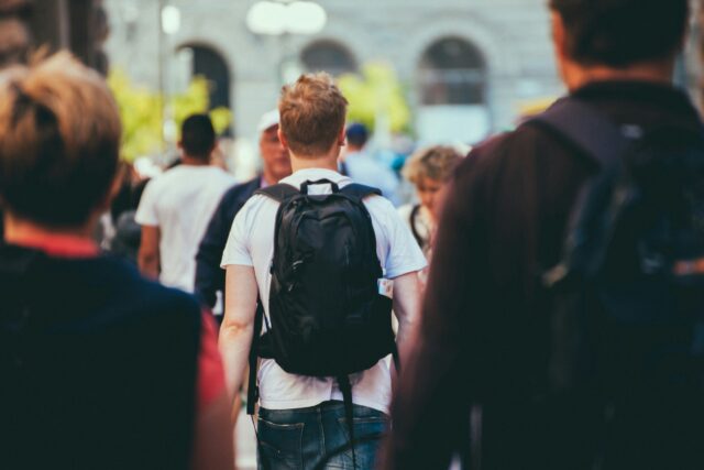 Un étudiant avec un sac à dos marchant sur le campus universitaire, entouré d’autres étudiants.