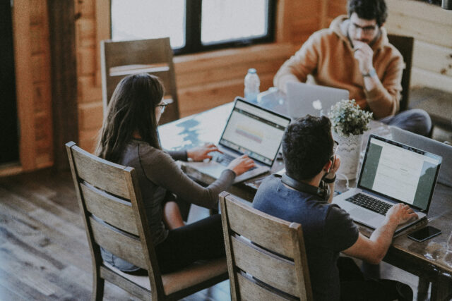 De jeunes adultes sur leurs ordinateurs portables assis autour d'une table.