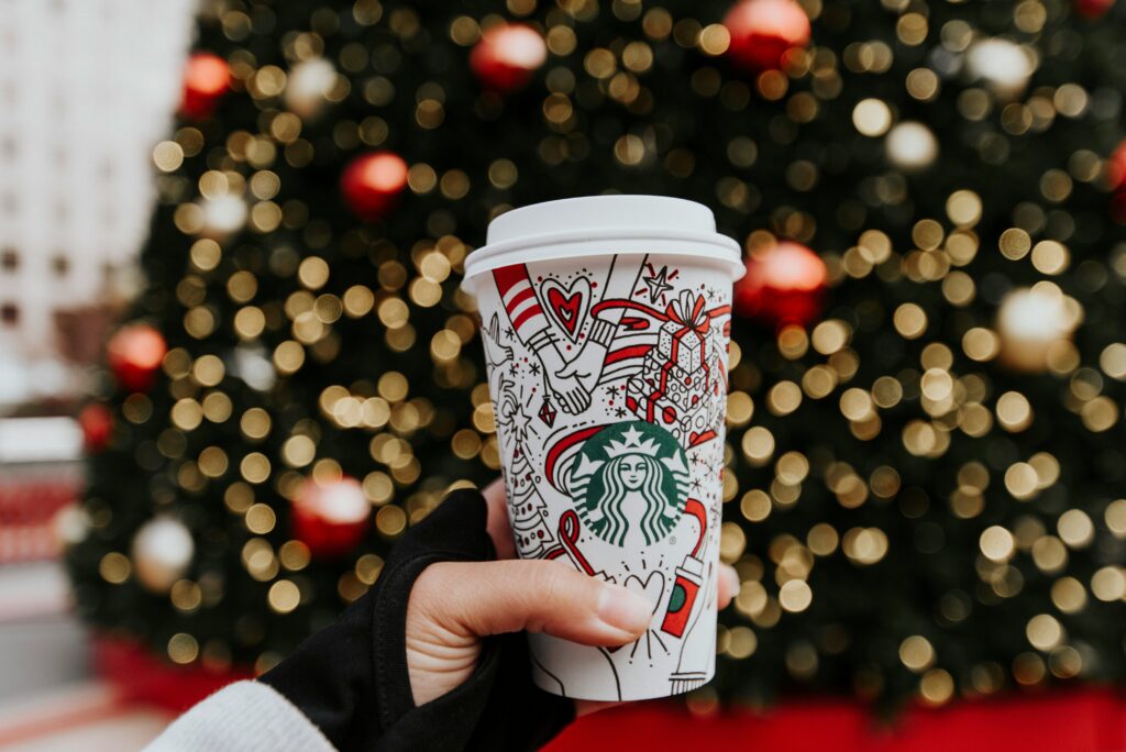 Quelqu'un tenant un café Starbucks devant un sapin de Noël.
