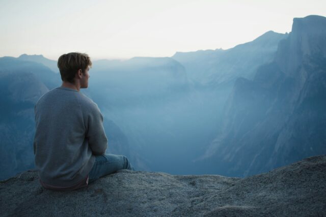 Un homme assis au bord d'une montagne regardant la vue.