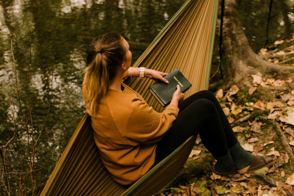 Une femme dans un hamac en forêt, tenant une Bible.