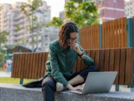 Une femme assise dehors cherchant des emplois sur son ordinateur portable.