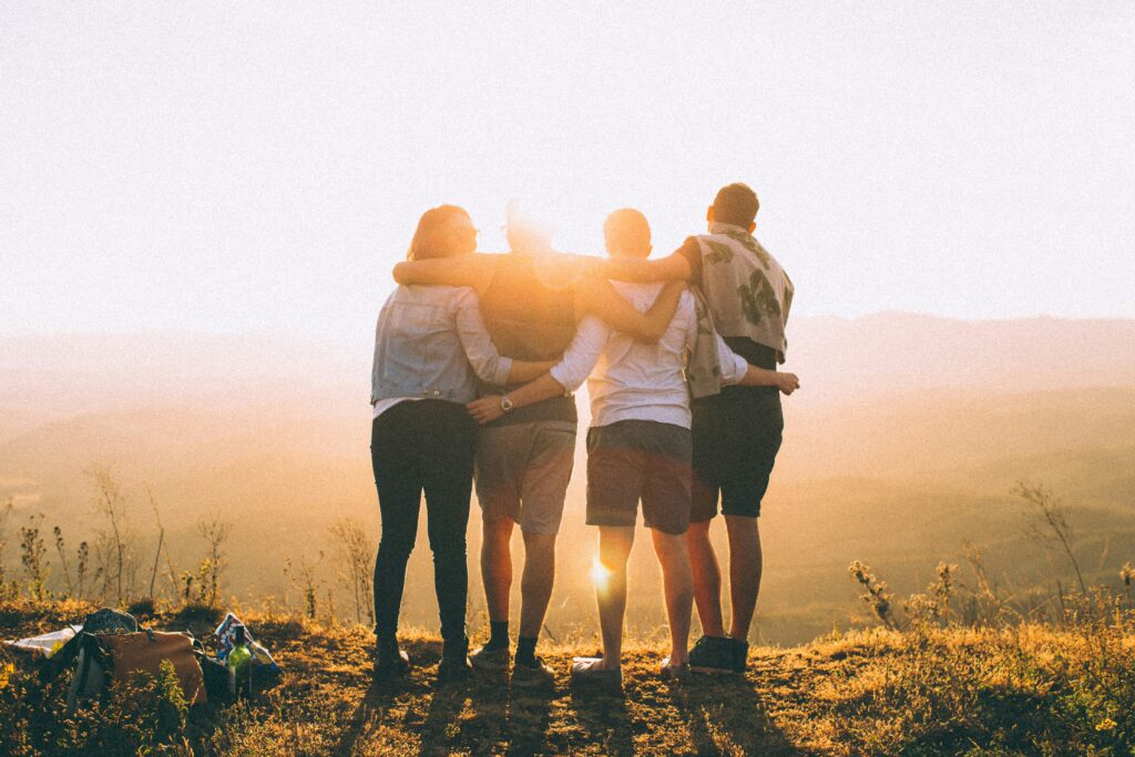Quatre personnes, bras dessus bras dessous, regardant le coucher du soleil.