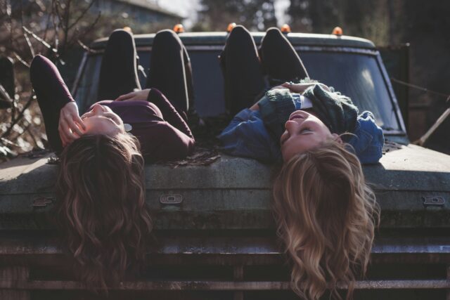 Deux jeunes femmes qui discutent allongées sur le capot d’un vieux camion.