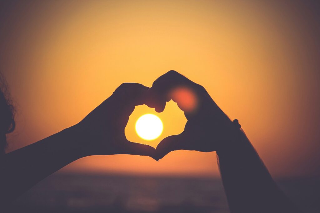 Une personne formant un cœur avec ses mains devant le soleil.