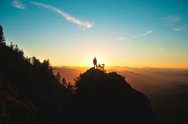 Un homme debout sur une montagne regardant le coucher du soleil.