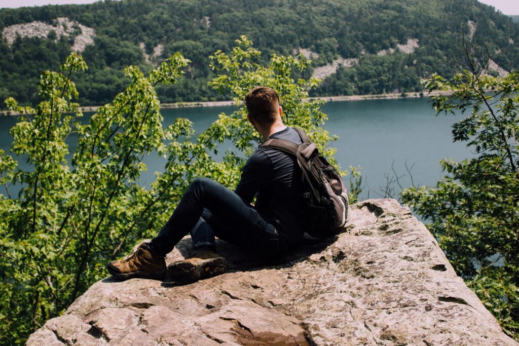 Un jeune homme assis dans la nature sur un rocher regardant l'eau.