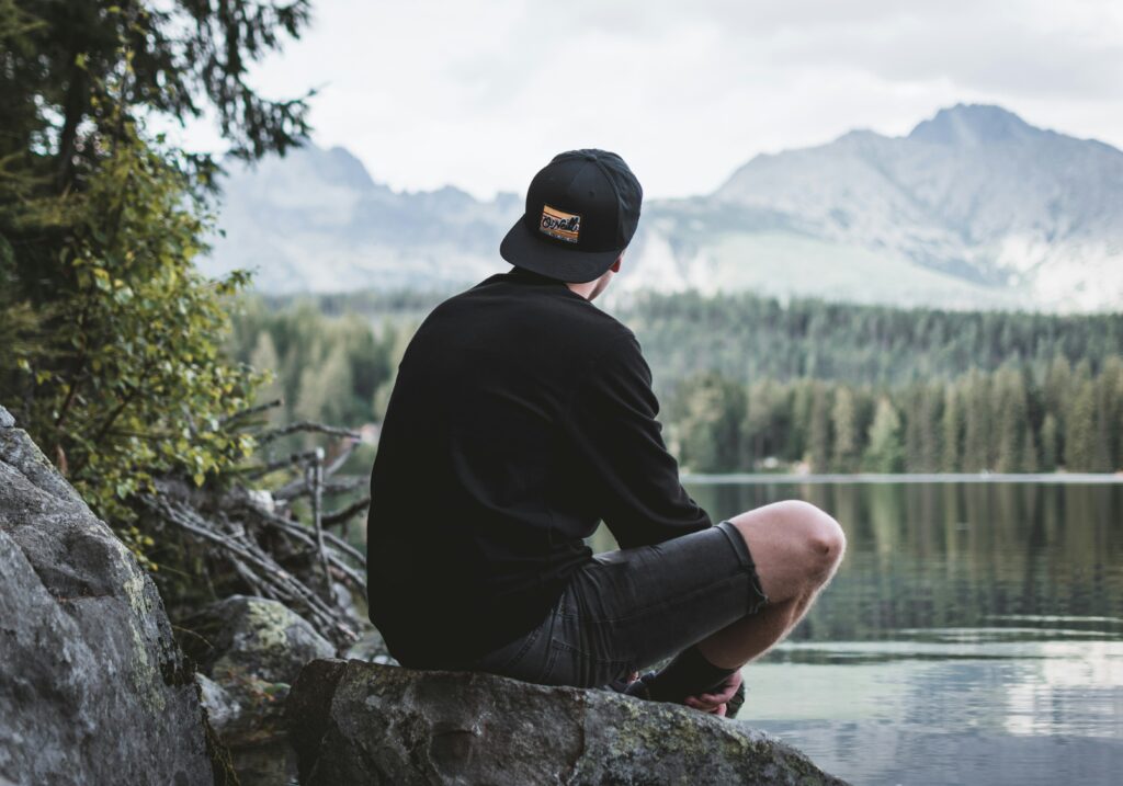 Un homme assis sur un rocher au bord de l'eau, regardant les montagnes.