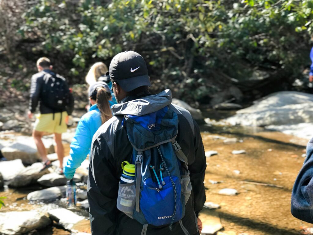 Des personnes avec des sacs à dos traversant un ruisseau.
