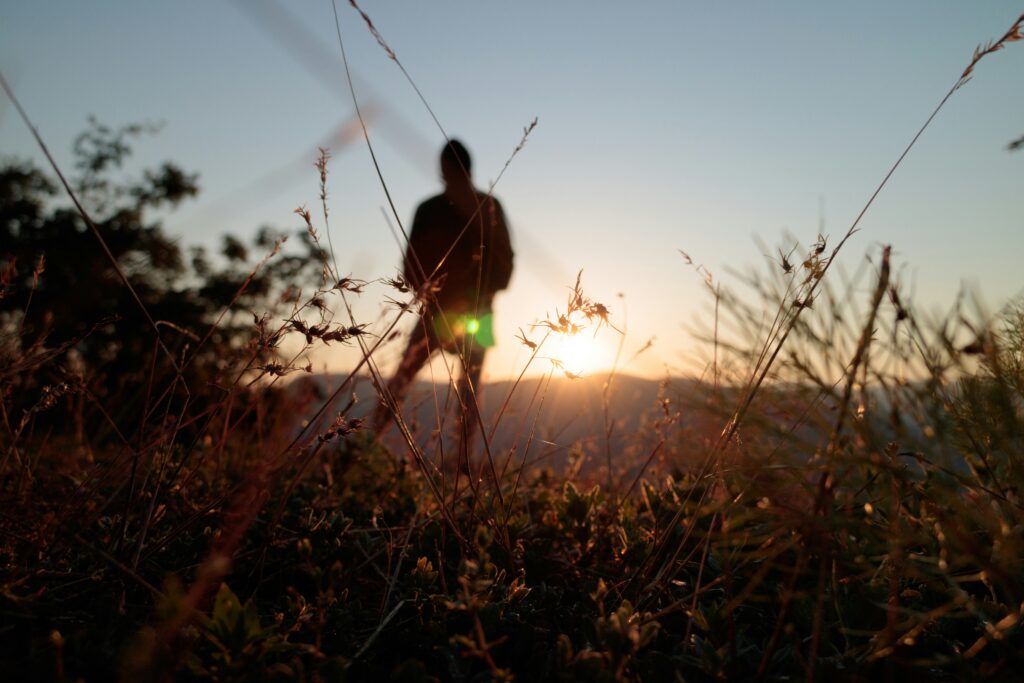 Un homme debout au loin dans un champ regardant le coucher du soleil.