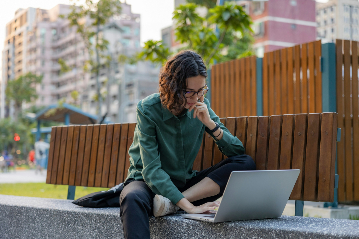Une femme assise dehors cherchant des emplois sur son ordinateur portable.
