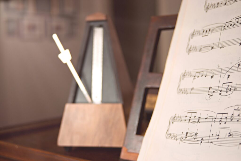 Un métronome qui tique à côté de partitions sur un piano.
