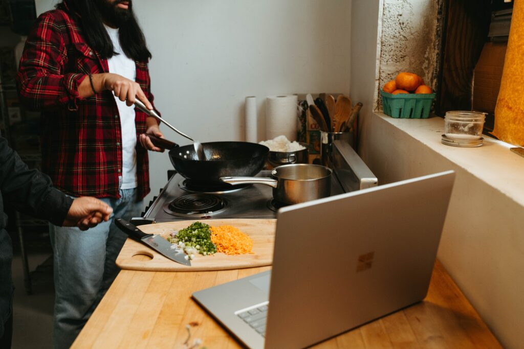 Deux personnes cuisinant et lisant la recette sur un ordinateur portable.