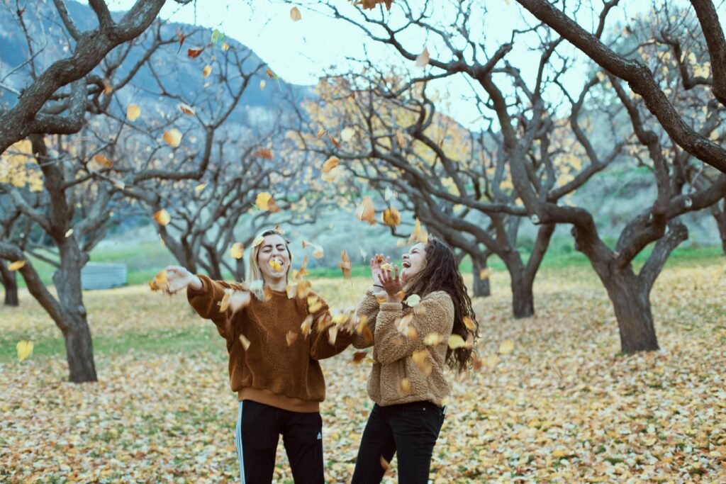 Deux femmes rient et lancent des feuilles.