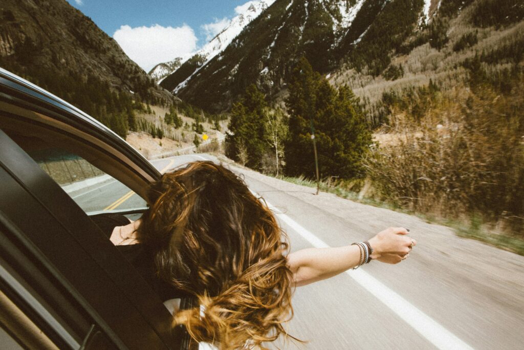Une femme dans une voiture, la tête sortie par la fenêtre, traversant les montagnes.