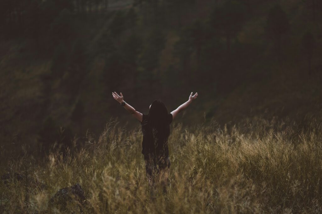 Une jeune femme levant les mains vers le ciel dans un champ.